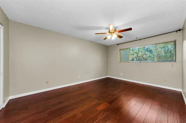 a view of an empty room with wooden floor and a ceiling fan