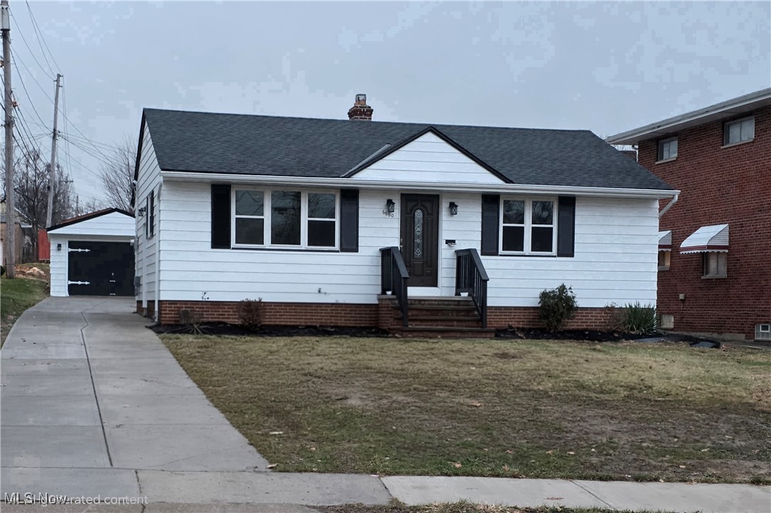 View of front of property featuring an outbuilding, a shingled roof, a chimney, and a front lawn