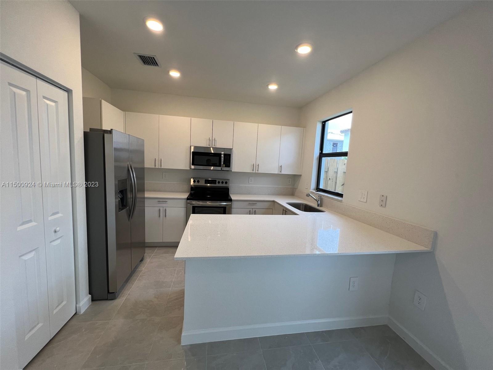 11743 Southwest 246th Terrace, Unit 11743 Homestead, FL 33032 - Photo 2 of 10 a kitchen with kitchen island a refrigerator and a stove top oven