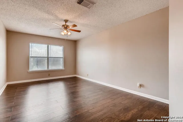 an empty room with wooden floor chandelier fan and windows