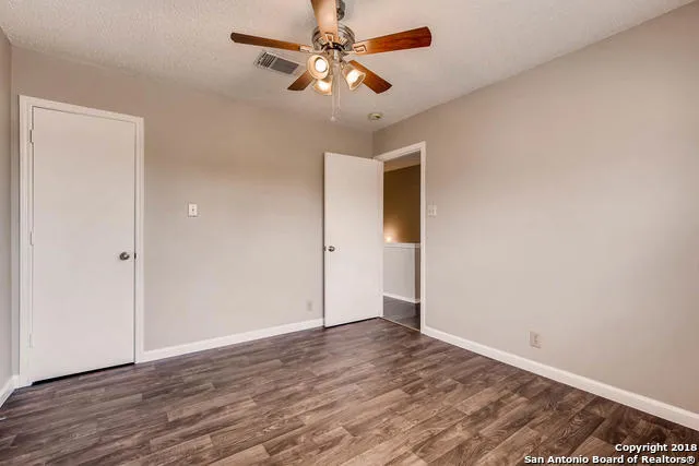 an empty room with wooden floor fan and windows