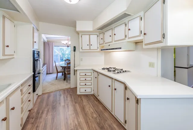 a kitchen with granite countertop a sink dishwasher stove and white cabinets with wooden floor
