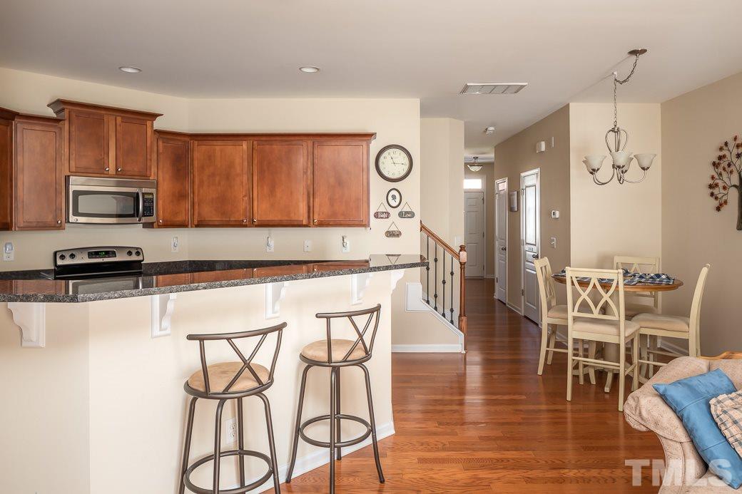 1345 Still Monument Way Raleigh, NC 27603 - Photo 8 of 28 a kitchen with stainless steel appliances granite countertop a stove top oven a sink a dining table and chairs with wooden floor