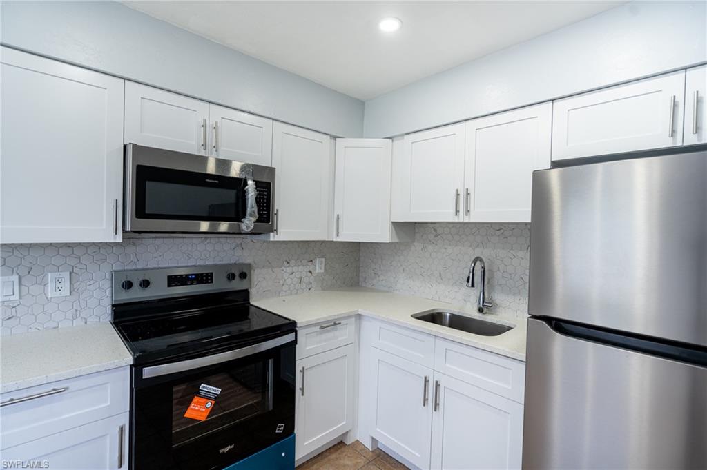 1940 48th Street Southwest Naples, FL 34116 - Photo 17 of 33 Kitchen featuring white shaker-style cabinetry, light-toned countertops, a geometric tile backsplash, stainless steel appliances, and a stainless steel sink with a gooseneck faucet