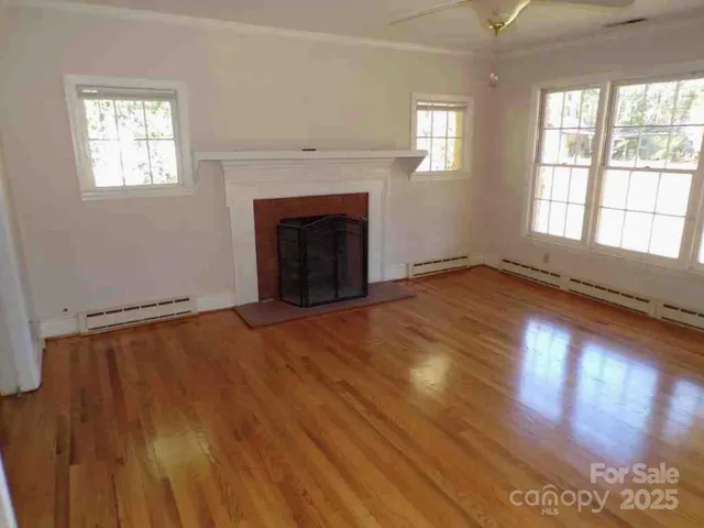 an empty room with wooden floor fireplace and windows
