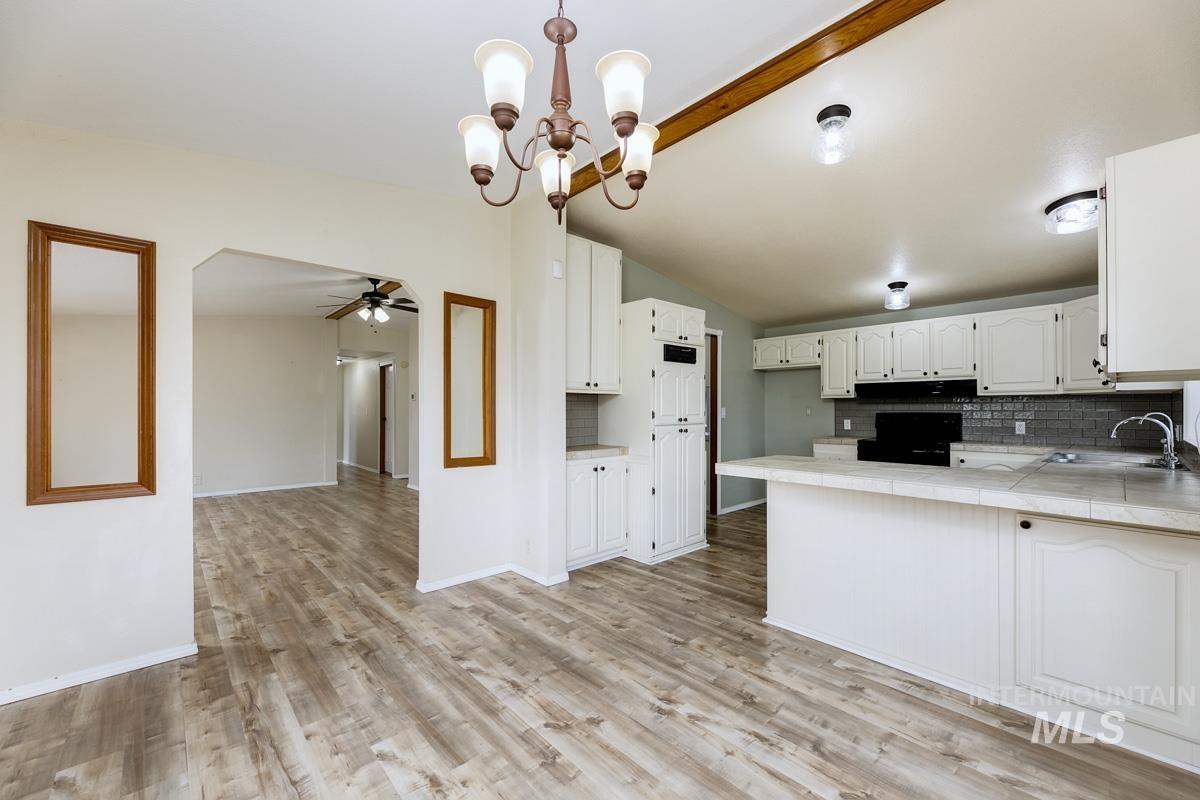 10131 Highway 44 Middleton, ID 83644 - Photo 13 of 42 Kitchen featuring tile counters, decorative backsplash, a chandelier, white cabinets, and lofted ceiling