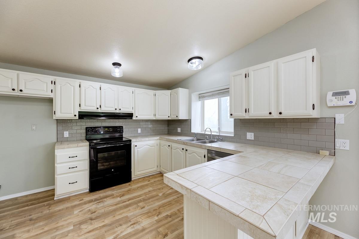 10131 Highway 44 Middleton, ID 83644 - Photo 14 of 42 Kitchen featuring black electric range oven, vaulted ceiling, white cabinetry, a peninsula, and tile countertops