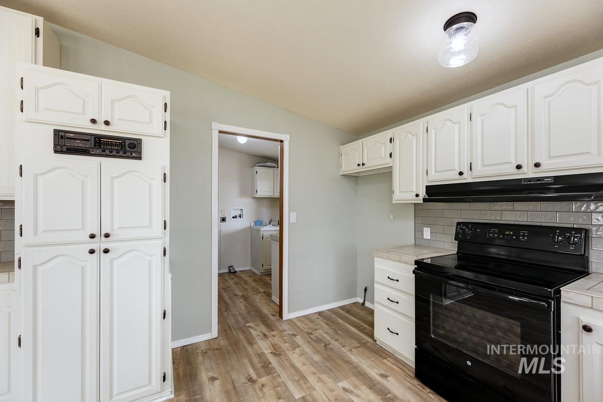 10131 Highway 44 Middleton, ID 83644 - Photo 16 of 42 Kitchen with electric range, tasteful backsplash, white cabinetry, vaulted ceiling, and light wood-style floors