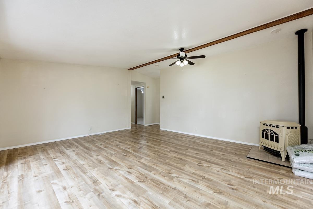 10131 Highway 44 Middleton, ID 83644 - Photo 9 of 42 Unfurnished room featuring a wood stove, a ceiling fan, lofted ceiling with beams, and light wood-style floors