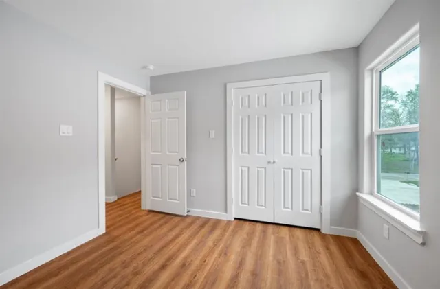 a view of an empty room with wooden floor and a window