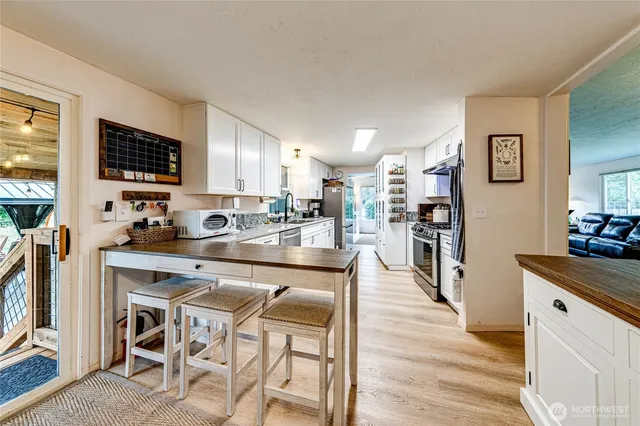 a kitchen with stainless steel appliances kitchen island granite countertop a refrigerator a stove a sink dishwasher and white cabinets with wooden floor