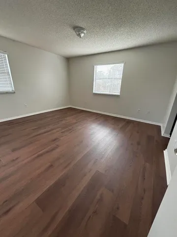 an empty room with wooden floor fan and windows