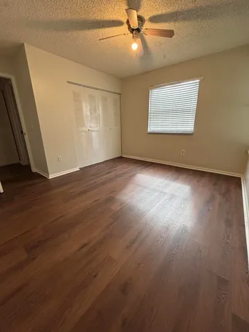 an empty room with wooden floor fan and windows