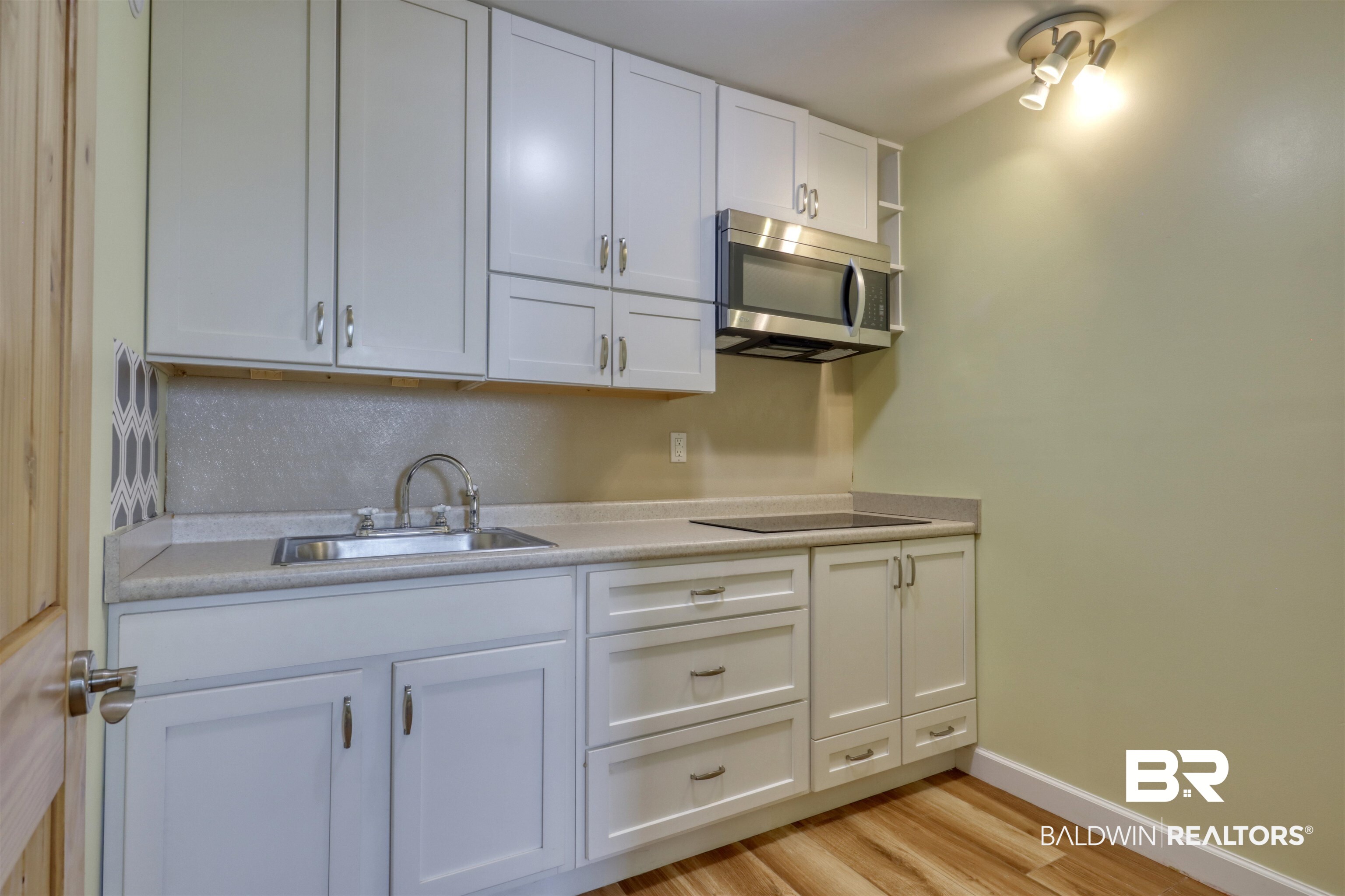 28461 Gardner Road Elberta, AL 36530 - Photo 25 of 46 Kitchen with white cabinetry, light countertops, stainless steel microwave, and light wood-style flooring