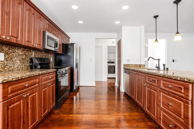 a kitchen with stainless steel appliances granite countertop a refrigerator a sink dishwasher and wooden cabinets with wooden floor