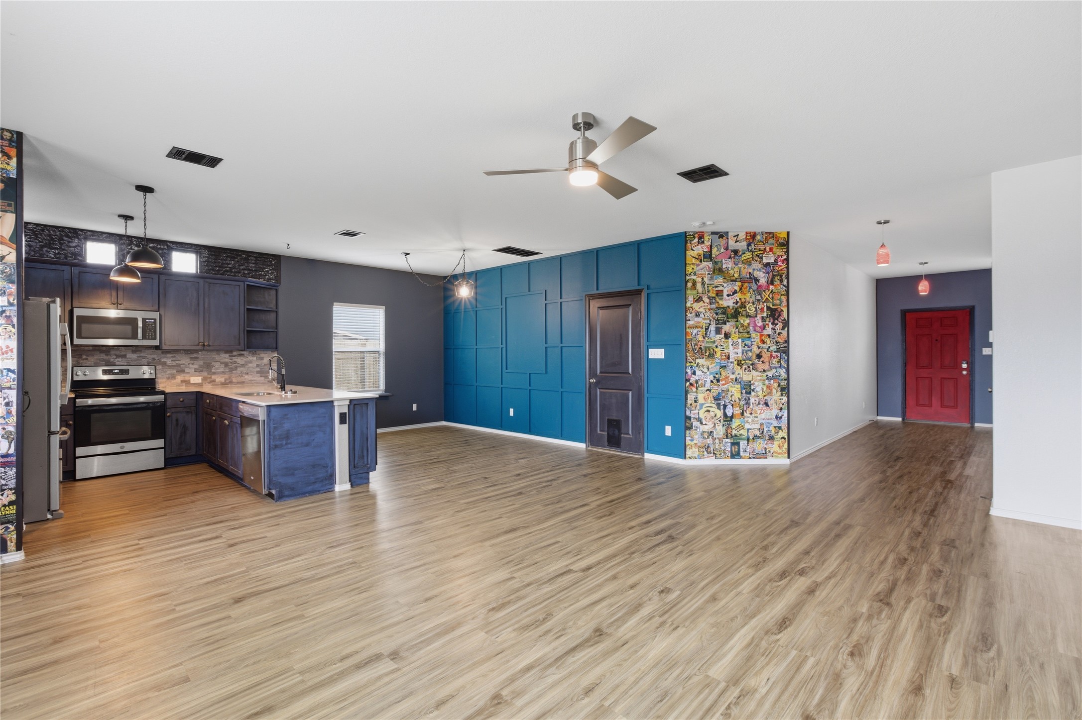 116 Night Riders Way Jarrell, TX 76537 - Photo 12 of 40 Open-concept interior featuring wood-finish flooring, a kitchen island with pendant lighting, stainless steel appliances, and a detailed accent wall with a hidden door