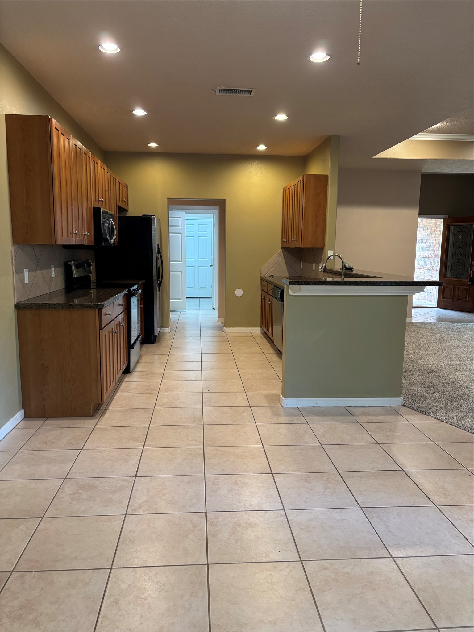 3238 Glenforest Road Montgomery, TX 77356 - Photo 13 of 41 This photo showcases a modern kitchen with ample wooden cabinetry, stainless steel appliances, and a sleek countertop. The space is well-lit with recessed lighting and features a tiled floor, opening into a carpeted living area.
