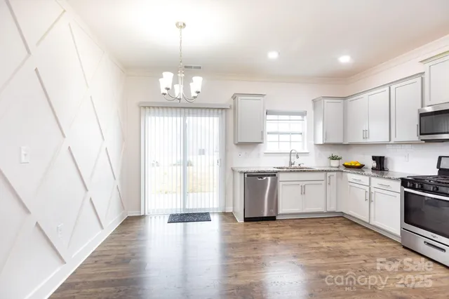 a kitchen with granite countertop a stove a sink dishwasher a refrigerator and white cabinets with wooden floor