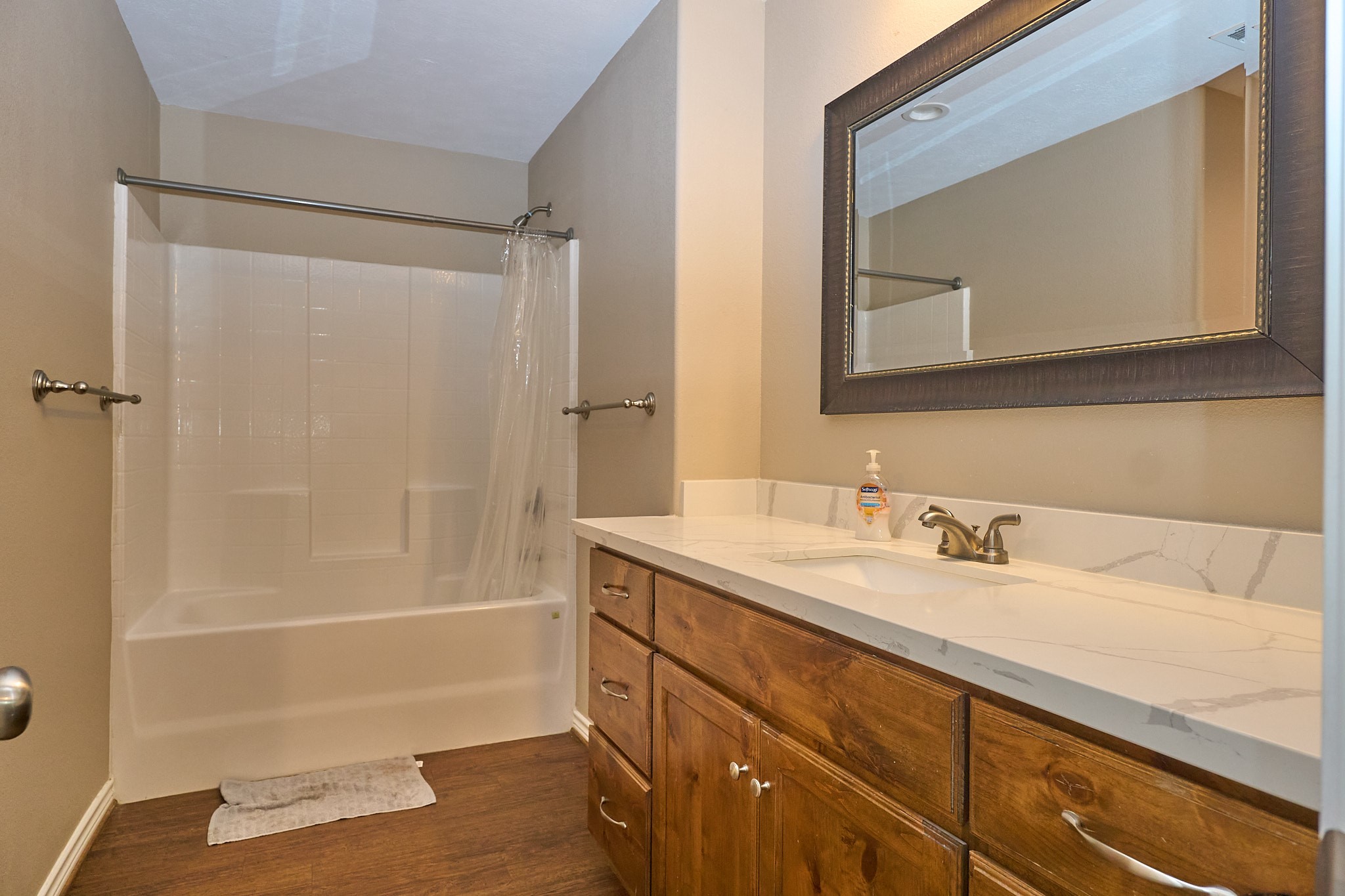 1807 Nuches Lane Bryan, TX 77803 - Photo 16 of 27 This bathroom features a classic design with a built-in tub and shower, a large vanity with a marble countertop, and a framed mirror. The warm wood cabinetry complements the neutral wall color, creating a cozy, inviting atmosphere.
