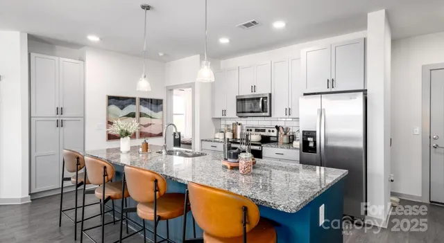 a kitchen with stainless steel appliances granite countertop a sink a stove a refrigerator cabinets and chairs