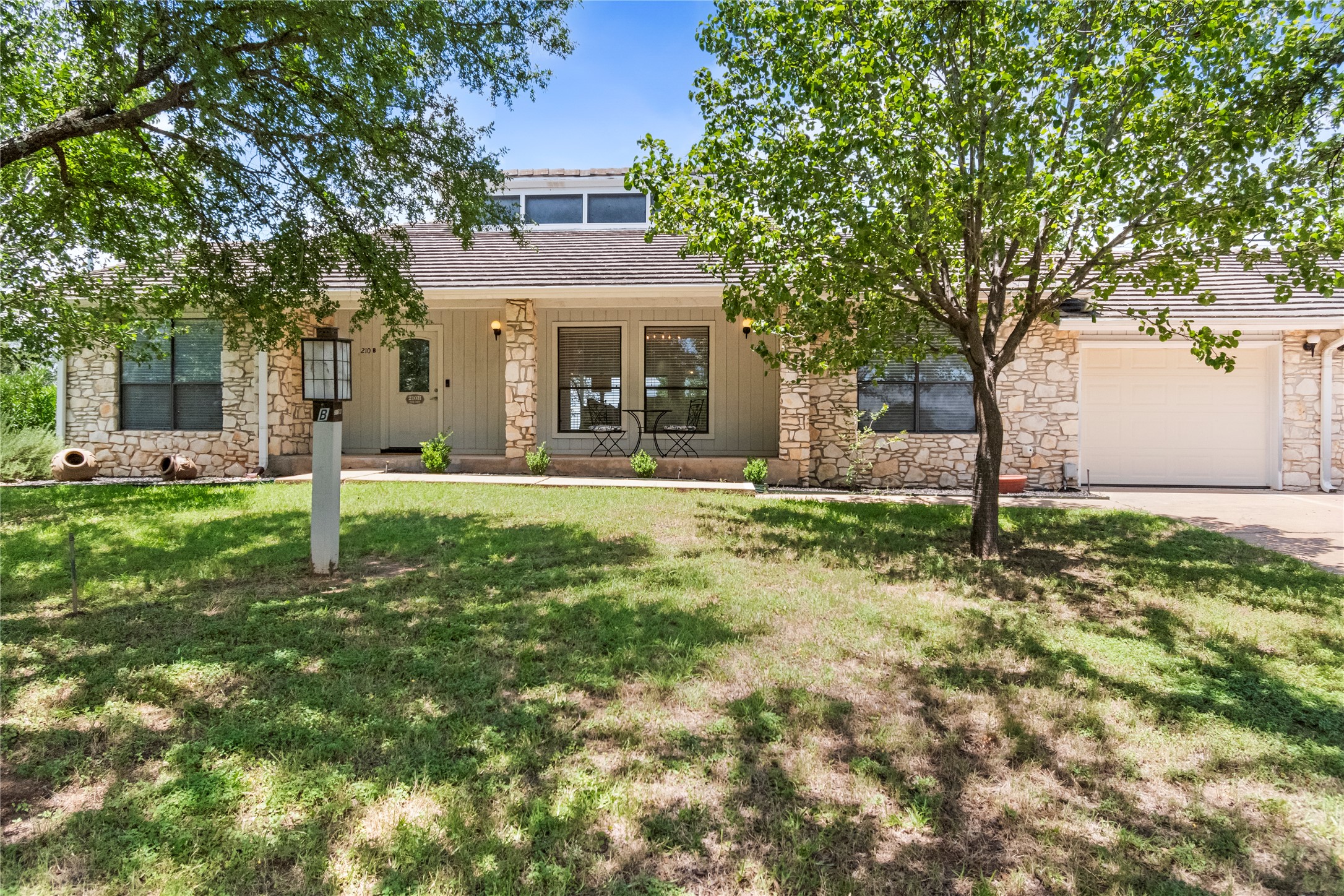 210 Teeoff, Unit B Horseshoe Bay, TX 78657 - Photo 2 of 38 An inviting stone-clad facade with a covered porch and mature trees creates a welcoming curb appeal.