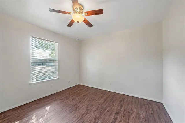 an empty room with wooden floor ceiling fan and window