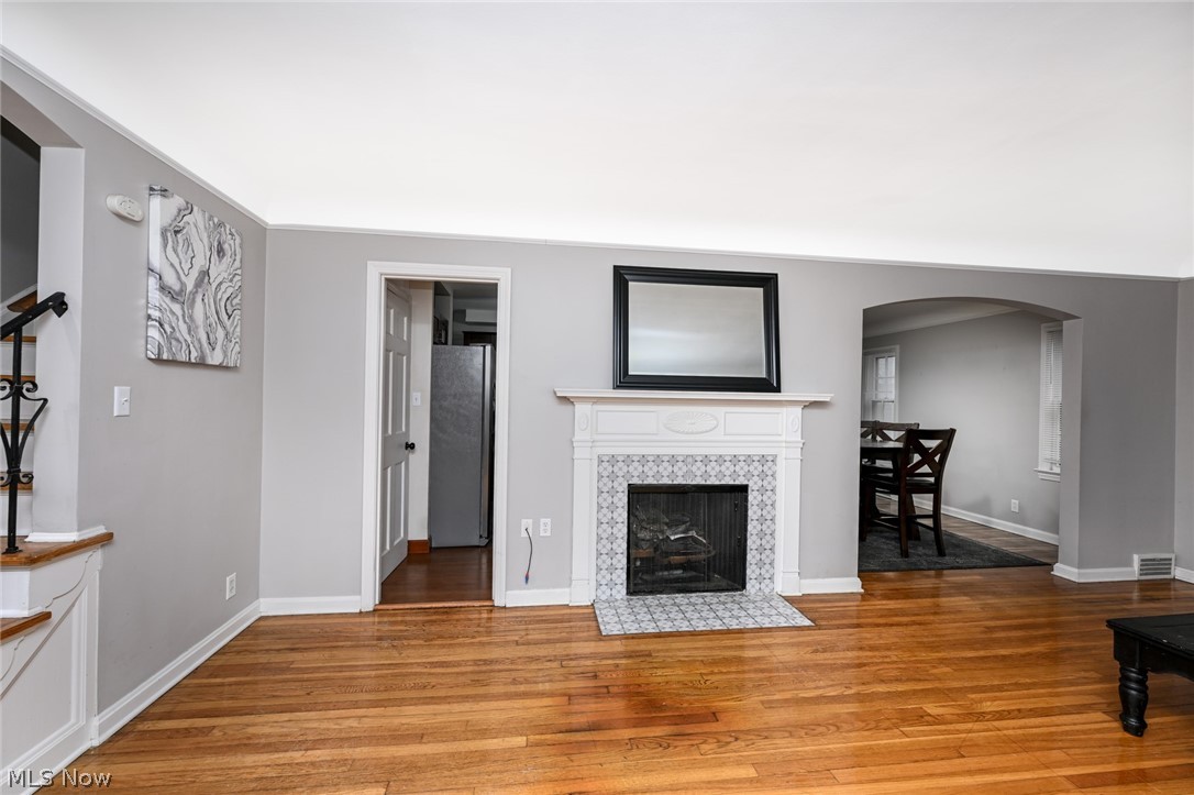 3699 Bainbridge Road Cleveland Heights, OH 44118 - Photo 7 of 37 Living area featuring wood-finish flooring, a white mantel fireplace with patterned tile surround, and an arched doorway