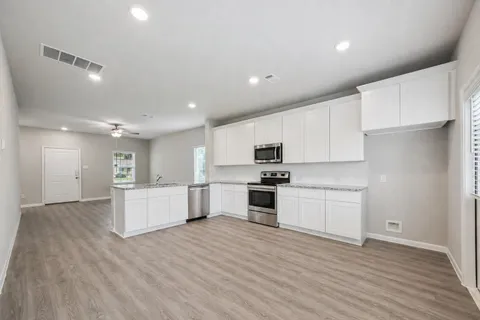 a large kitchen with kitchen island a sink a stove a refrigerator and white cabinets with wooden floor