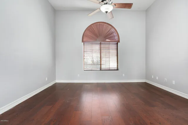 an empty room with wooden floor fan and windows