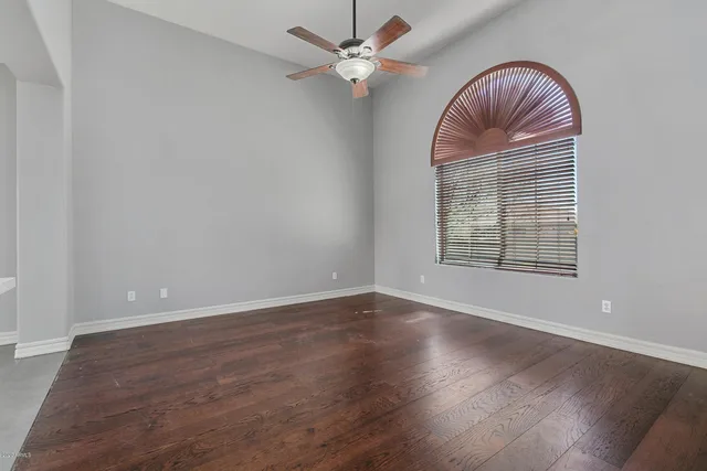 an empty room with wooden floor chandelier fan and windows