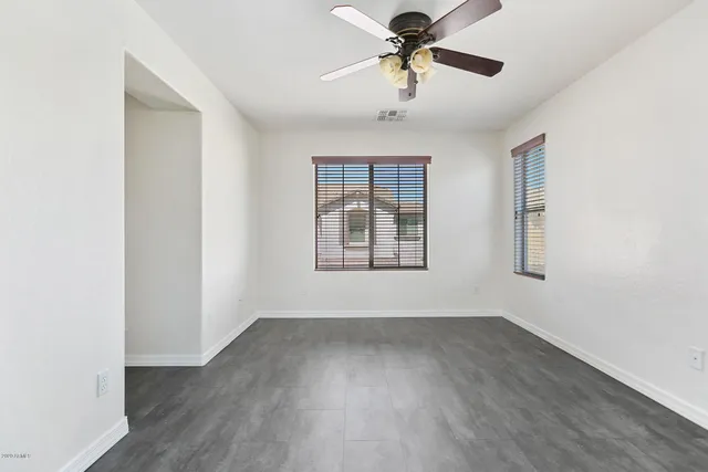 an empty room with wooden floor ceiling fan and windows