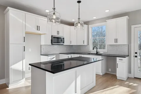 a kitchen that has a sink a microwave oven a stove and white cabinets with wooden floor