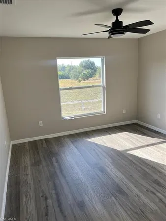 an empty room with wooden floor a ceiling fan and windows