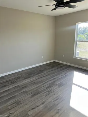 an empty room with wooden floor fan and windows