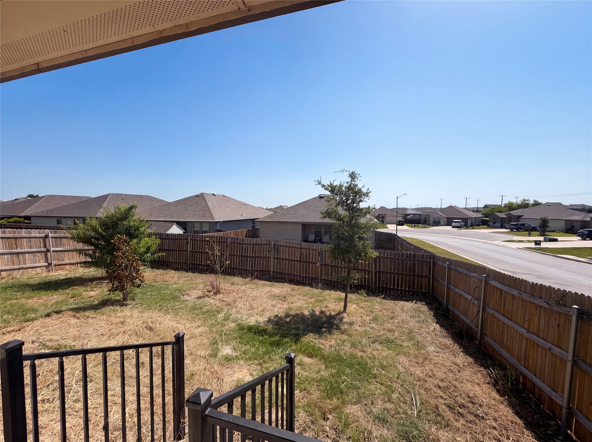 Wooden fencing encloses the yard, bordering a quiet neighborhood street under open blue skies.