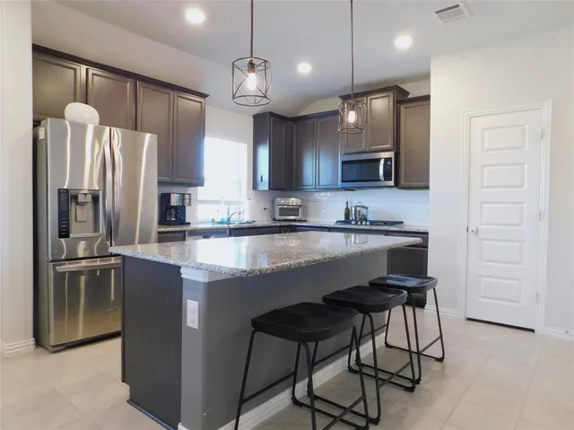 a kitchen with stainless steel appliances granite countertop a stove a refrigerator a kitchen island a sink cabinets and a refrigerator