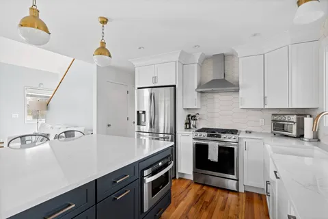 a kitchen with stainless steel appliances a sink dishwasher a stove and white cabinets with wooden floor