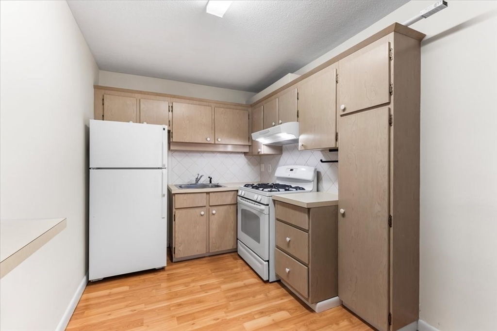 4925 Washington Street, Unit 304 Boston, MA 02132 - Photo 6 of 25 a kitchen with white cabinets and white appliances