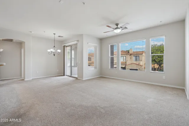 an empty room with chandelier fan and windows