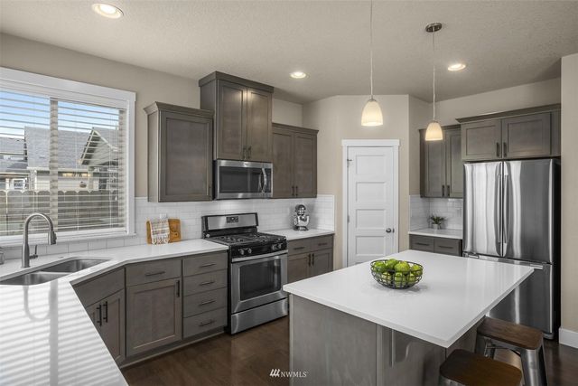 a kitchen with stainless steel appliances granite countertop a sink a stove a refrigerator a center island and a cabinets