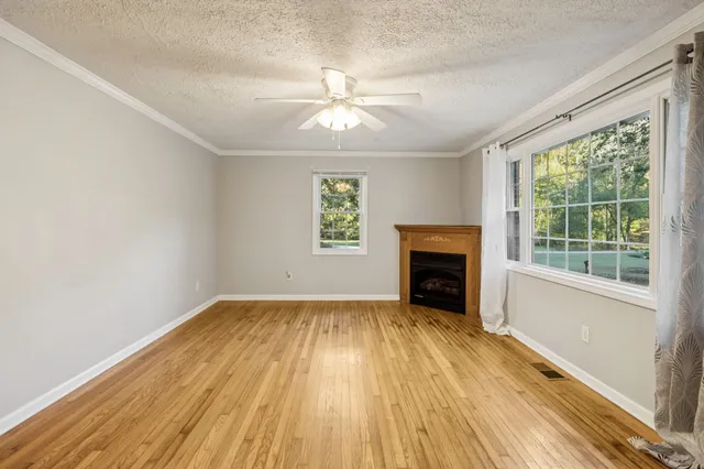 a view of an empty room with wooden floor fireplace and a window