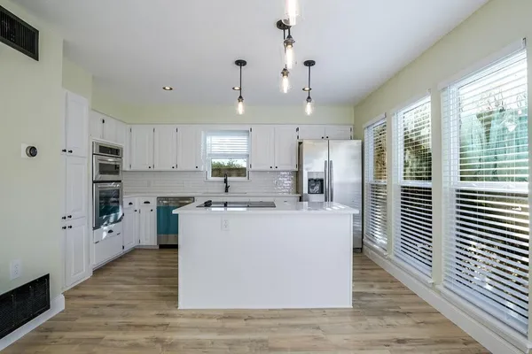 a large kitchen with stainless steel appliances a large counter top a stove a refrigerator cabinets and a window