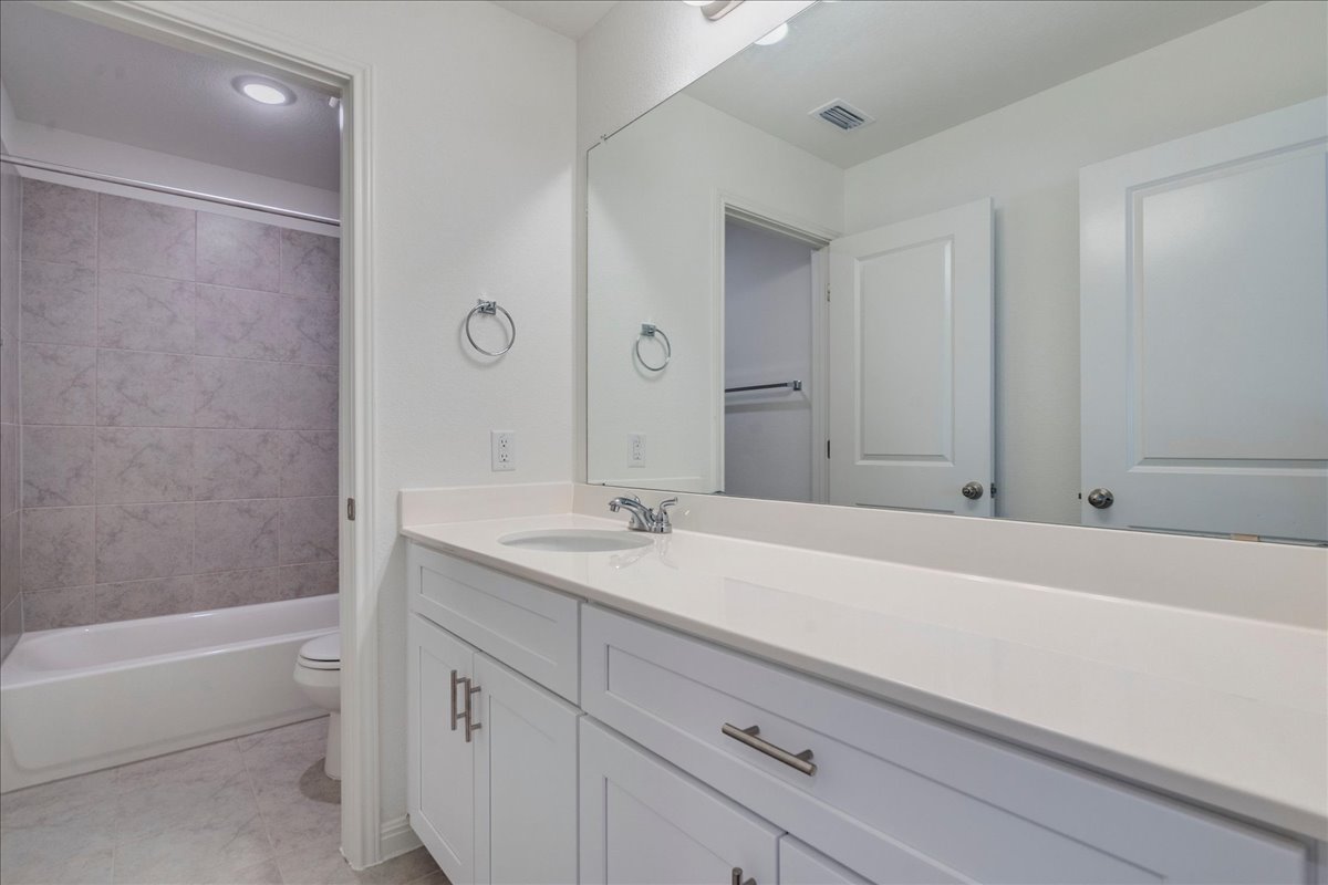 223 Rieber Road Kyle, TX 78640 - Photo 23 of 40 An expansive mirror sits above a sleek vanity adjacent to a tiled tub enclosure.