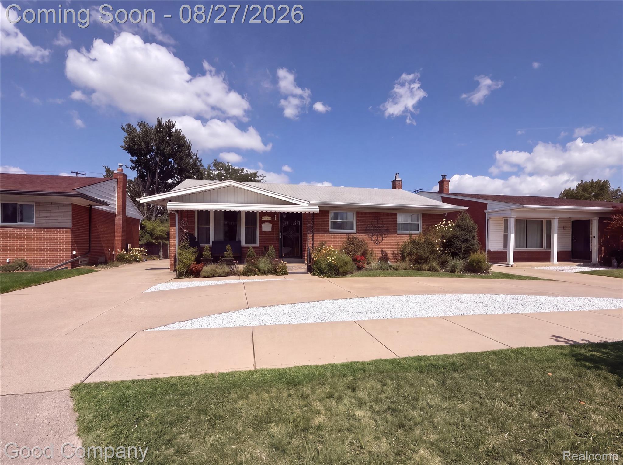 Brick exterior with white trim, covered front entry, concrete driveway, and mature landscaping