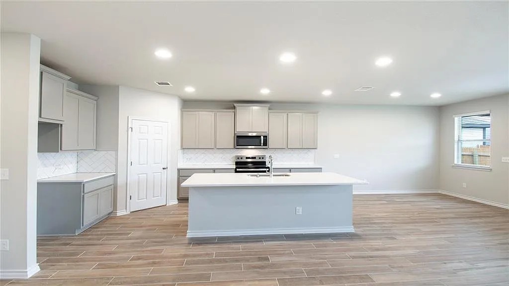317 Capstone Road Liberty Hill, TX 78642 - Photo 8 of 10 Kitchen featuring gray cabinetry, a kitchen island with sink, appliances with stainless steel finishes, recessed lighting, and wood tiled floors