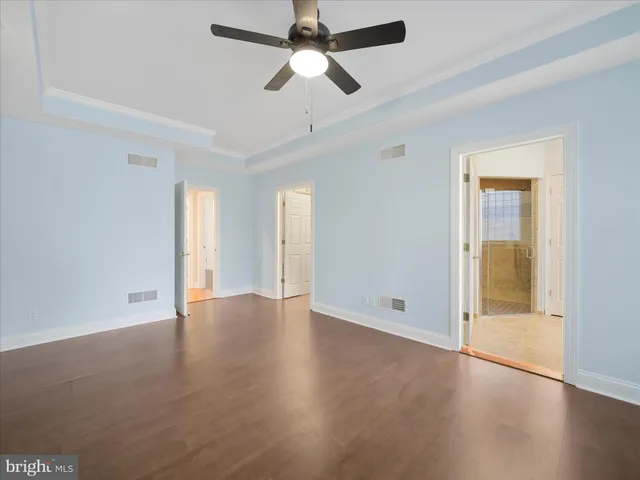 a view of an empty room with wooden floor and a ceiling fan