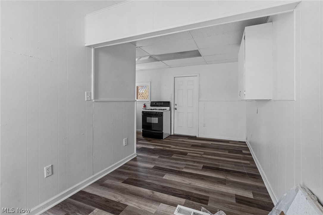 2387 29th Street Southwest Akron, OH 44314 - Photo 11 of 24 Kitchen featuring white cabinetry, range with gas stovetop, dark wood-style flooring, wooden walls, and light countertops