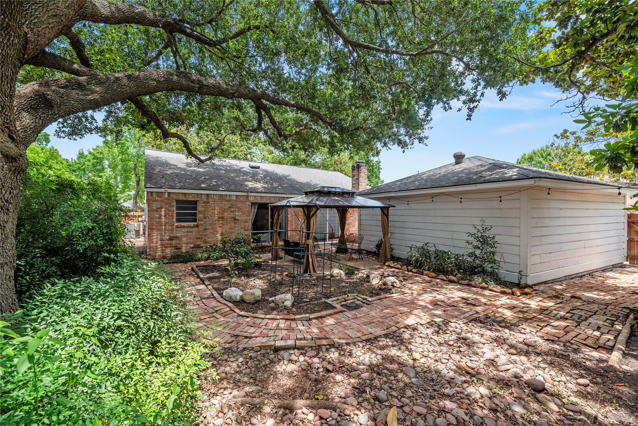 14203 Wickersham Lane Houston, TX 77077 - Photo 22 of 25 Rear exterior angle highlighting the brick construction of the home, its low-maintenance shingle roof, and the seamless integration of the patio areas with the detached garage structure.