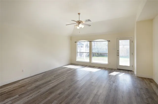 an empty room with wooden floor fan and windows
