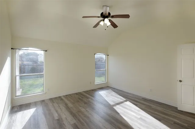 an empty room with wooden floor fan and windows